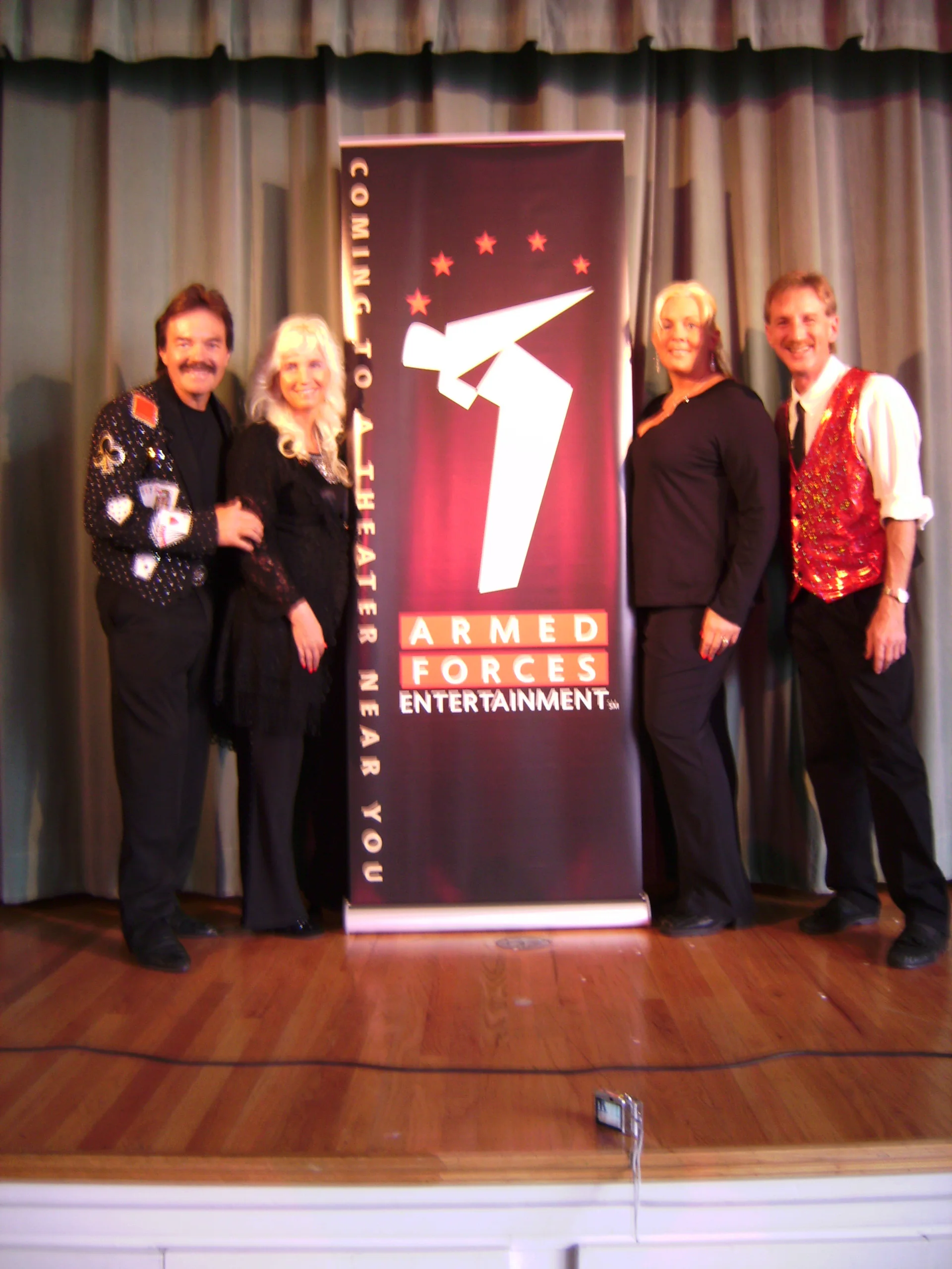 Rick Moore, Donna Moore, Crystal Stupar, Rodney Kelley standing onstage with Armed Forces sign in Aviano, Italy